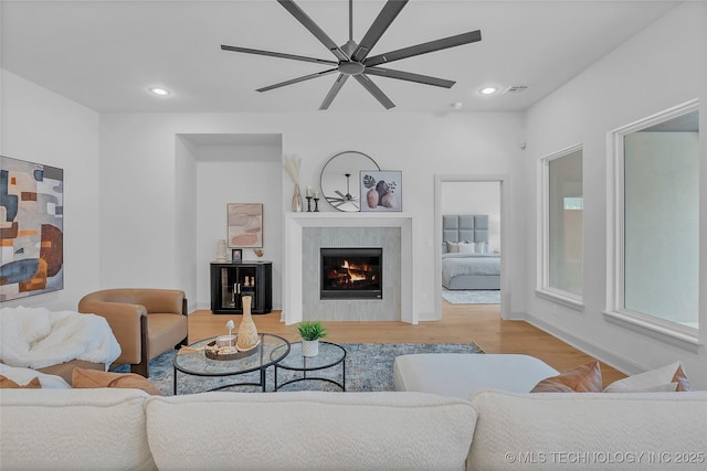 living room featuring ceiling fan, a tile fireplace, and light hardwood / wood-style flooring