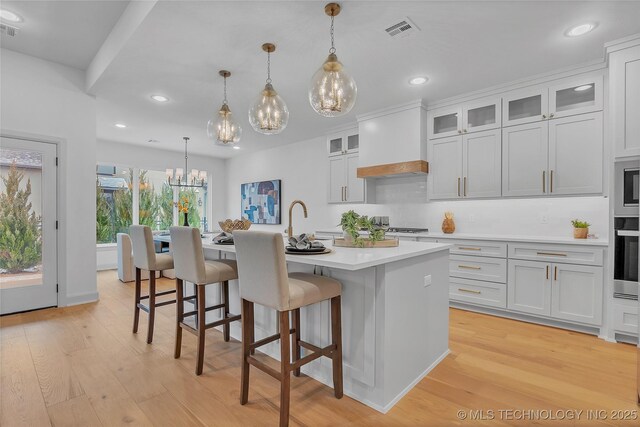 kitchen with pendant lighting, white cabinetry, a center island with sink, and custom range hood