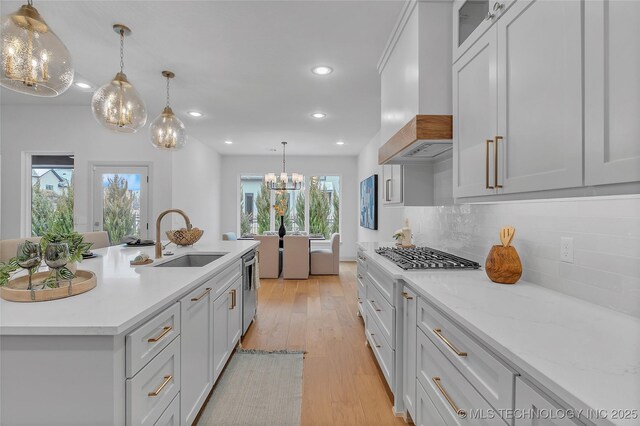 kitchen with custom exhaust hood, white cabinets, sink, decorative light fixtures, and backsplash