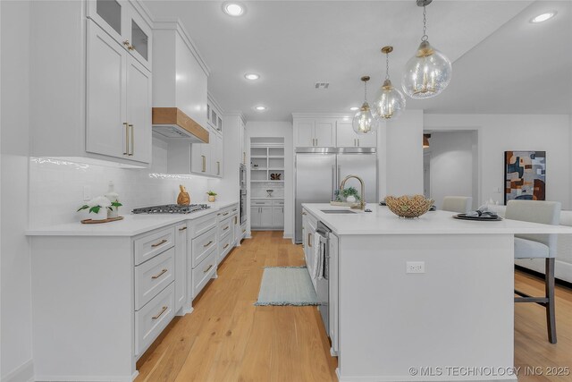 kitchen featuring decorative light fixtures, stainless steel appliances, a center island with sink, white cabinets, and sink