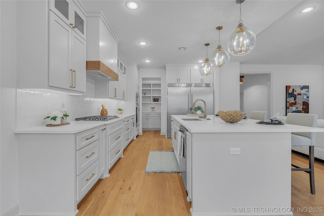 kitchen with sink, pendant lighting, stainless steel appliances, a kitchen island with sink, and white cabinets