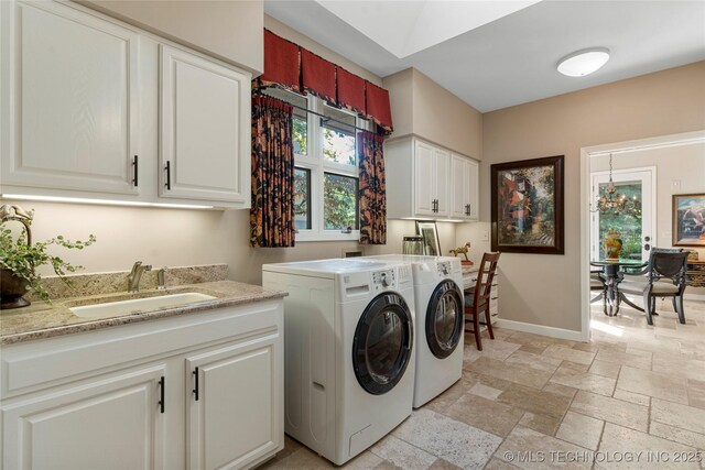 washroom featuring sink, washing machine and clothes dryer, a notable chandelier, and cabinets