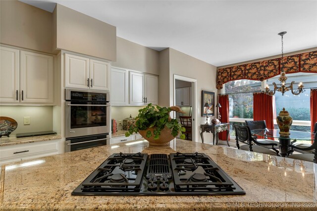 kitchen featuring hanging light fixtures, black gas cooktop, stainless steel double oven, light stone counters, and an inviting chandelier