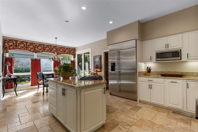 kitchen with built in appliances, light stone countertops, a notable chandelier, pendant lighting, and white cabinets