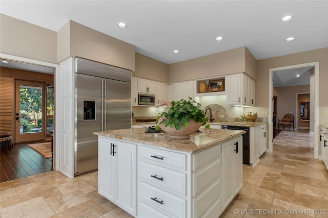 kitchen with built in appliances, light stone countertops, a kitchen island, white cabinets, and sink