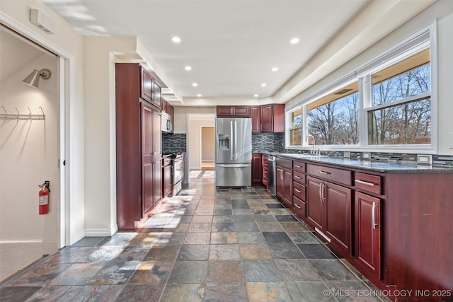 kitchen with sink, dark stone counters, appliances with stainless steel finishes, and decorative backsplash