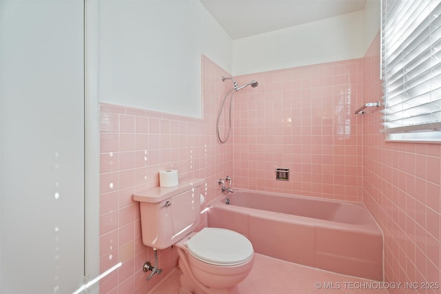 bathroom featuring tile patterned flooring, tiled shower / bath combo, toilet, tile walls, and a healthy amount of sunlight