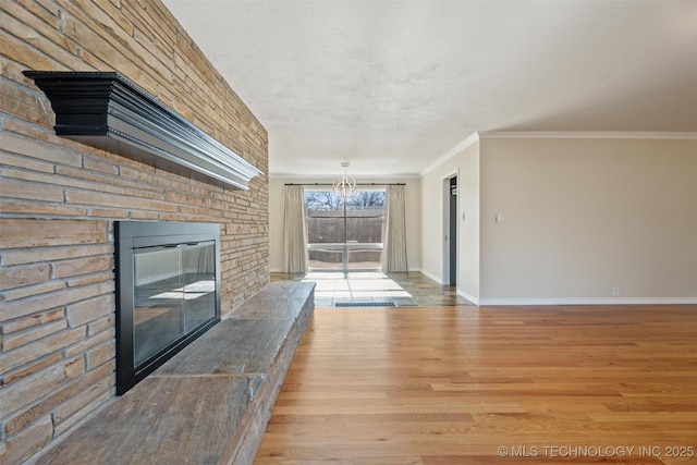 unfurnished living room with crown molding, a large fireplace, a notable chandelier, and light hardwood / wood-style flooring