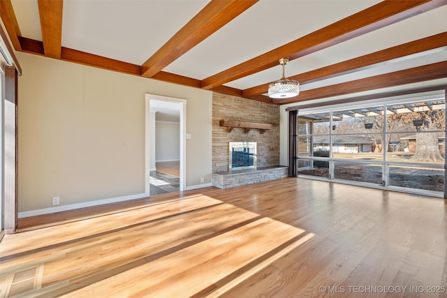 unfurnished living room featuring hardwood / wood-style flooring, beamed ceiling, and a stone fireplace