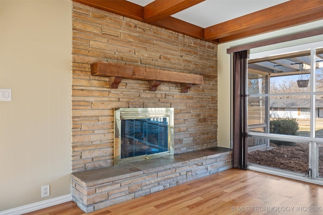 unfurnished living room with light hardwood / wood-style floors, beamed ceiling, and a stone fireplace