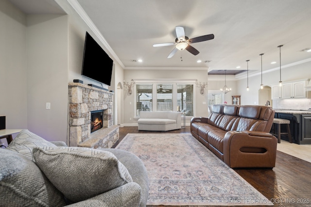 living room with ceiling fan with notable chandelier, a fireplace, dark wood-type flooring, and crown molding