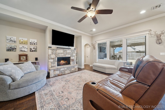 living room with dark hardwood / wood-style flooring, ceiling fan, crown molding, and a stone fireplace