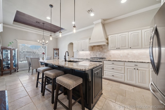 kitchen featuring a center island with sink, stainless steel appliances, premium range hood, sink, and white cabinetry