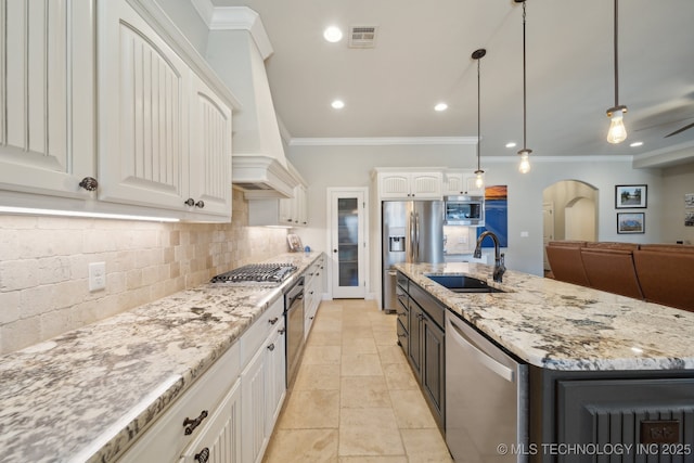 kitchen with decorative light fixtures, a center island with sink, white cabinetry, appliances with stainless steel finishes, and sink