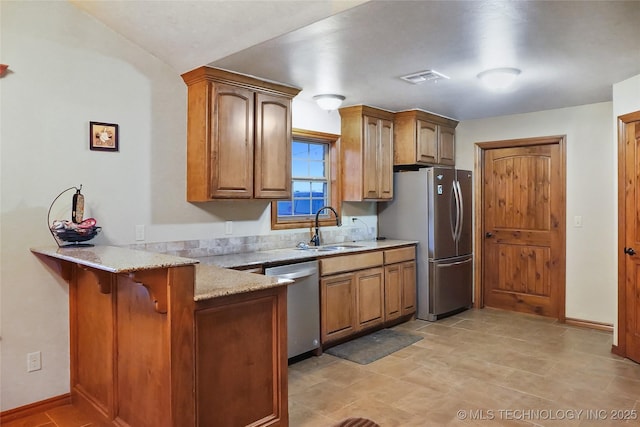 kitchen with stainless steel appliances, sink, kitchen peninsula, light stone counters, and a breakfast bar