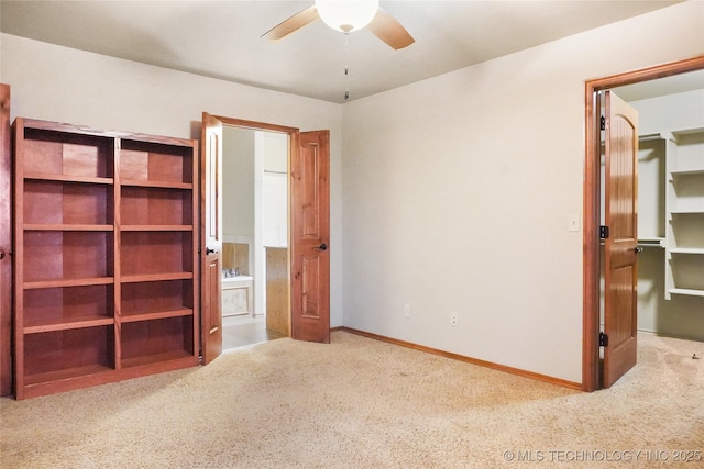 unfurnished bedroom featuring ceiling fan, ensuite bathroom, a spacious closet, and light carpet