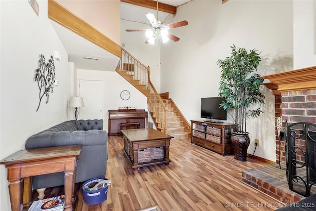 living room with hardwood / wood-style flooring, high vaulted ceiling, beam ceiling, a fireplace, and ceiling fan