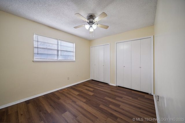 unfurnished bedroom with ceiling fan, dark hardwood / wood-style flooring, two closets, and a textured ceiling