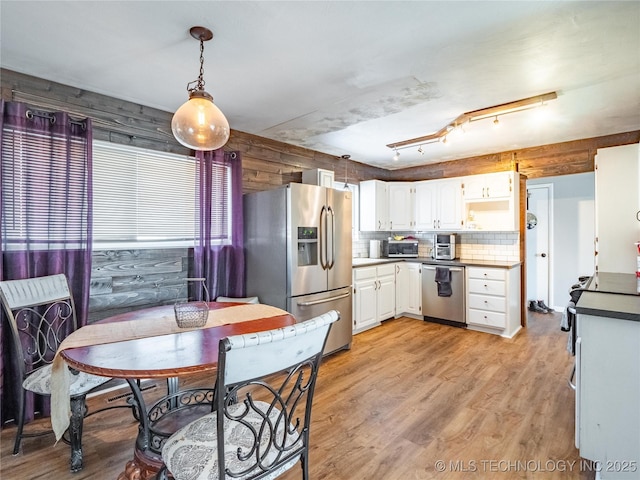 kitchen featuring decorative light fixtures, white cabinetry, light wood-type flooring, backsplash, and appliances with stainless steel finishes