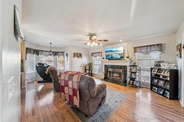 living room featuring hardwood / wood-style floors, a fireplace, ceiling fan, and a textured ceiling