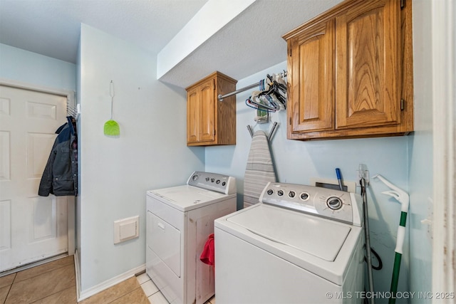 laundry area with light tile patterned flooring, washing machine and clothes dryer, a textured ceiling, and cabinets