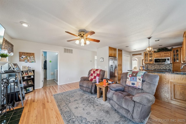 living room with ceiling fan, light wood-type flooring, and a textured ceiling