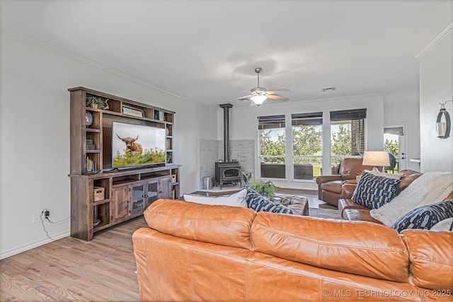 living room featuring ceiling fan, light wood-type flooring, crown molding, and a wood stove