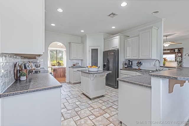 kitchen featuring a center island, kitchen peninsula, ceiling fan, decorative backsplash, and black fridge with ice dispenser