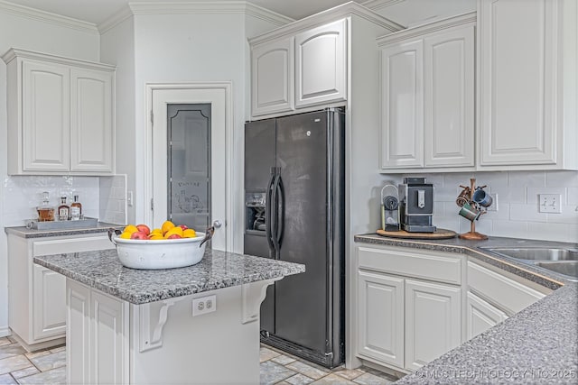 kitchen with black fridge with ice dispenser, white cabinetry, backsplash, and crown molding