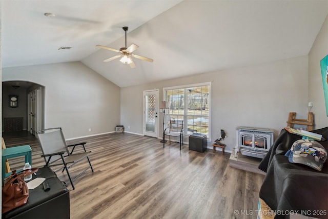 living area featuring ceiling fan, hardwood / wood-style floors, vaulted ceiling, and a wood stove