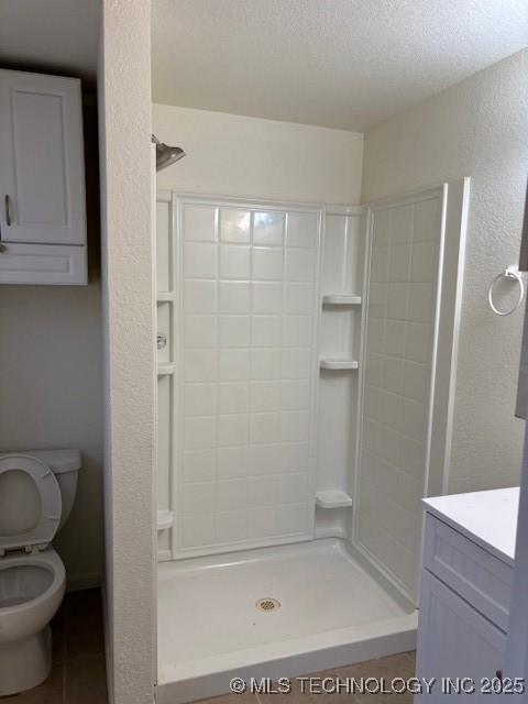 bathroom with tile patterned flooring, toilet, vanity, a shower, and a textured ceiling