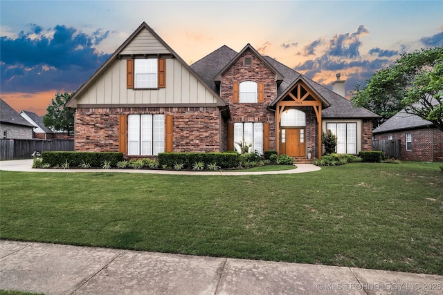 craftsman-style house with a chimney, fence, brick siding, board and batten siding, and a yard