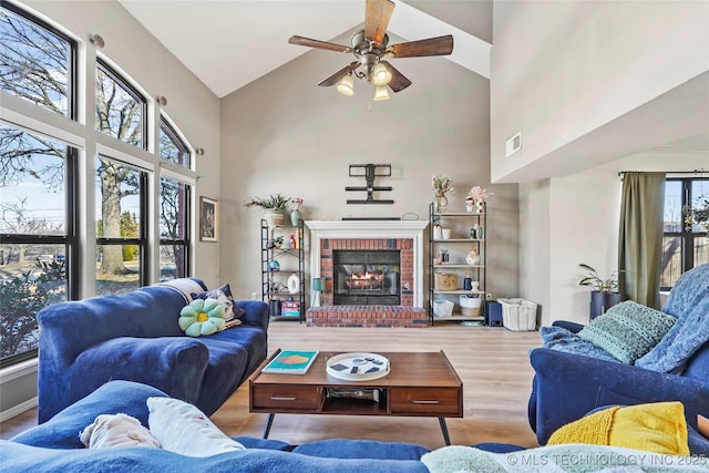 living room with high vaulted ceiling, a brick fireplace, hardwood / wood-style floors, and ceiling fan