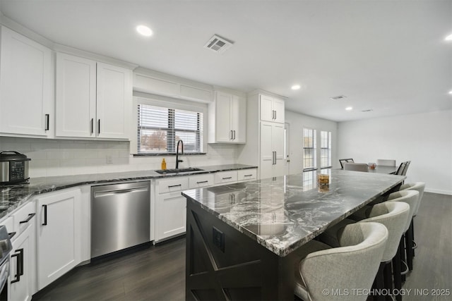 kitchen featuring stainless steel dishwasher, dark hardwood / wood-style floors, white cabinets, dark stone counters, and sink