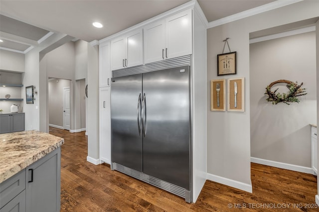 kitchen featuring built in fridge, white cabinetry, ornamental molding, light stone countertops, and dark hardwood / wood-style floors