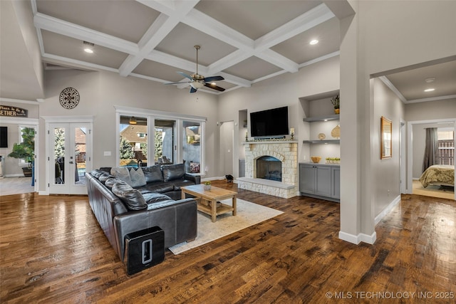 living room with a stone fireplace, french doors, ceiling fan, dark hardwood / wood-style flooring, and beam ceiling