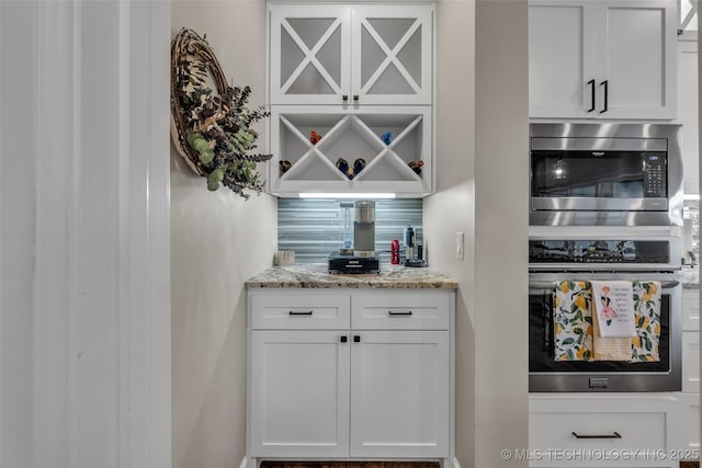 bar with appliances with stainless steel finishes, white cabinets, backsplash, and light stone counters