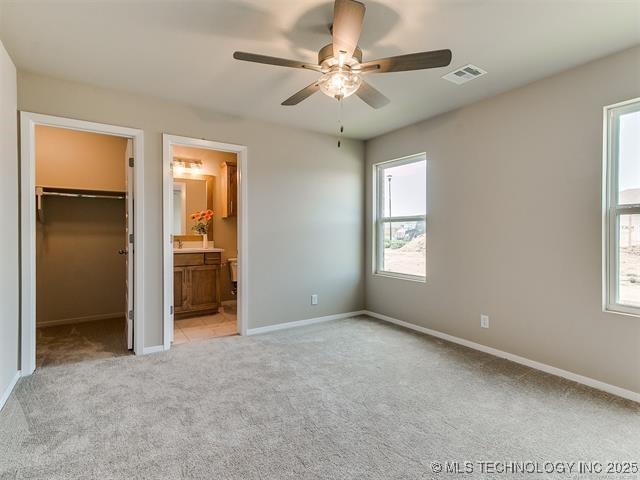 unfurnished bedroom featuring ensuite bath, ceiling fan, a spacious closet, and light carpet