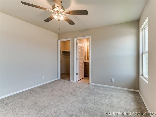 unfurnished bedroom featuring a closet, light carpet, ceiling fan, a spacious closet, and ensuite bathroom