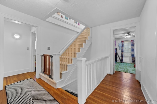 staircase featuring a textured ceiling, ceiling fan, and wood-type flooring