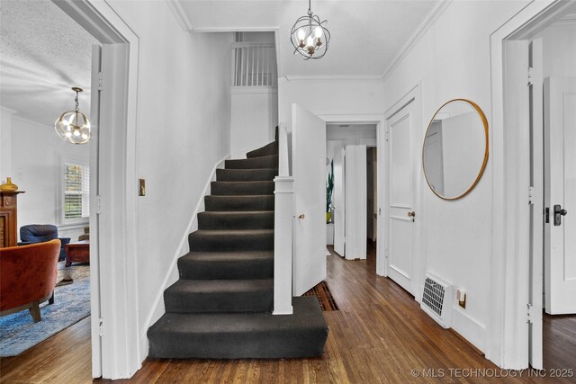 foyer entrance featuring a textured ceiling, dark hardwood / wood-style flooring, ornamental molding, and a notable chandelier