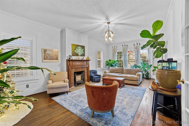 living room with a brick fireplace, a notable chandelier, dark wood-type flooring, a textured ceiling, and crown molding