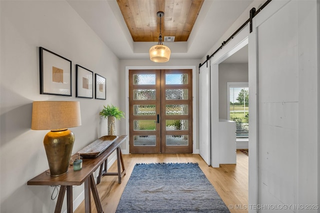 entryway with a raised ceiling, french doors, wood ceiling, light wood-type flooring, and a barn door