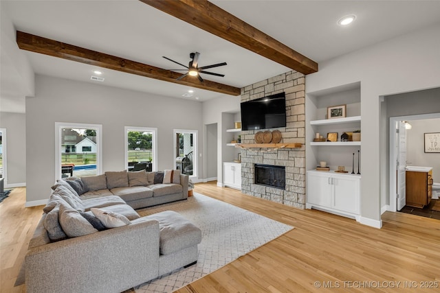 living room with a fireplace, ceiling fan, light wood-type flooring, built in shelves, and beam ceiling