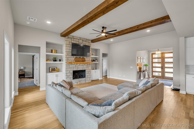 living room with french doors, built in shelves, light wood-type flooring, ceiling fan, and a stone fireplace