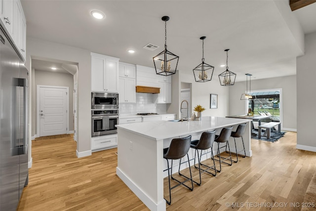 kitchen with white cabinetry, hanging light fixtures, an island with sink, and built in appliances