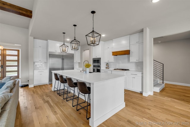 kitchen with built in appliances, a large island, beam ceiling, and white cabinetry