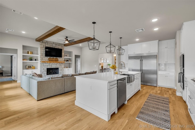 kitchen with beamed ceiling, white cabinets, built in appliances, and a center island with sink