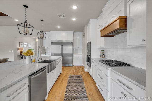 kitchen featuring sink, built in appliances, decorative light fixtures, and white cabinetry