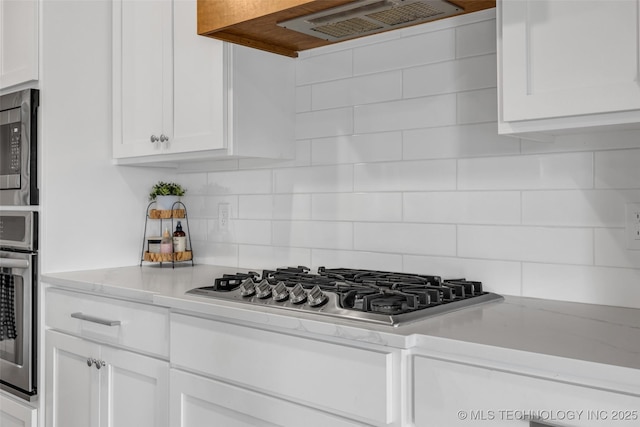 kitchen featuring wall chimney exhaust hood, decorative backsplash, and white cabinetry